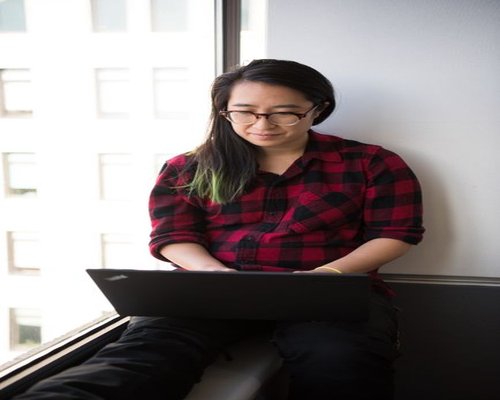 A person looking out of the window while working on a laptop